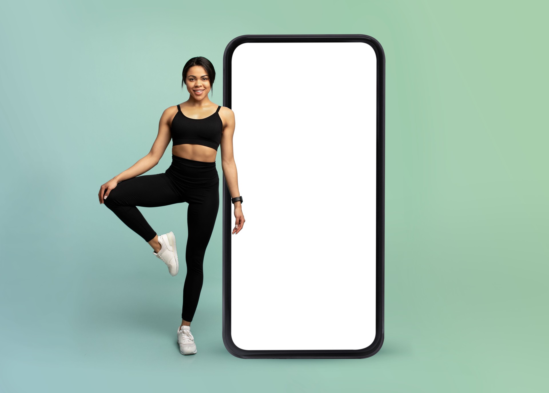 Mobile app for online workout. Young fitness lady standing near huge smartphone with white blank screen, mockup