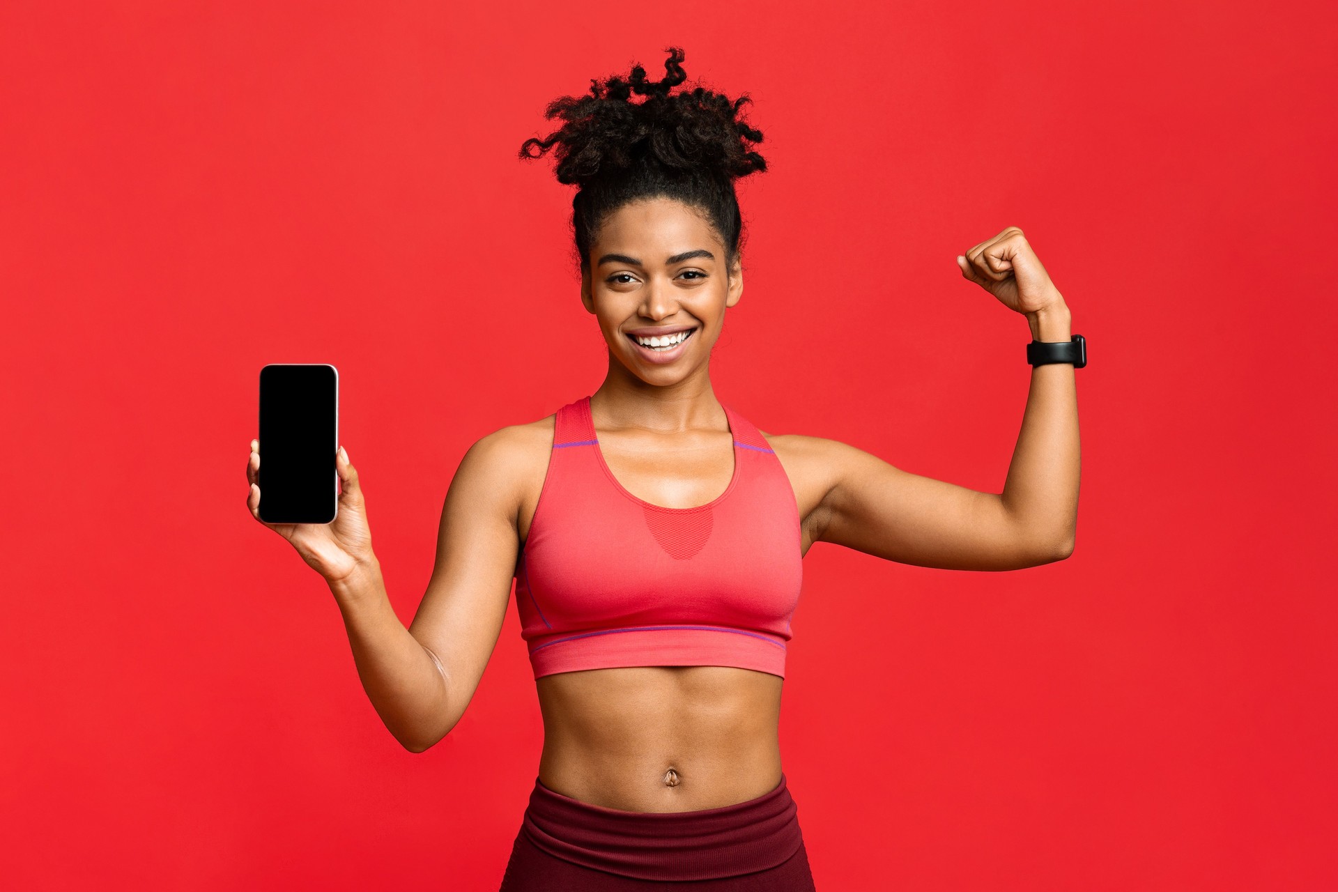 Sporty black girl showing smartphone blank screen and flexing muscles