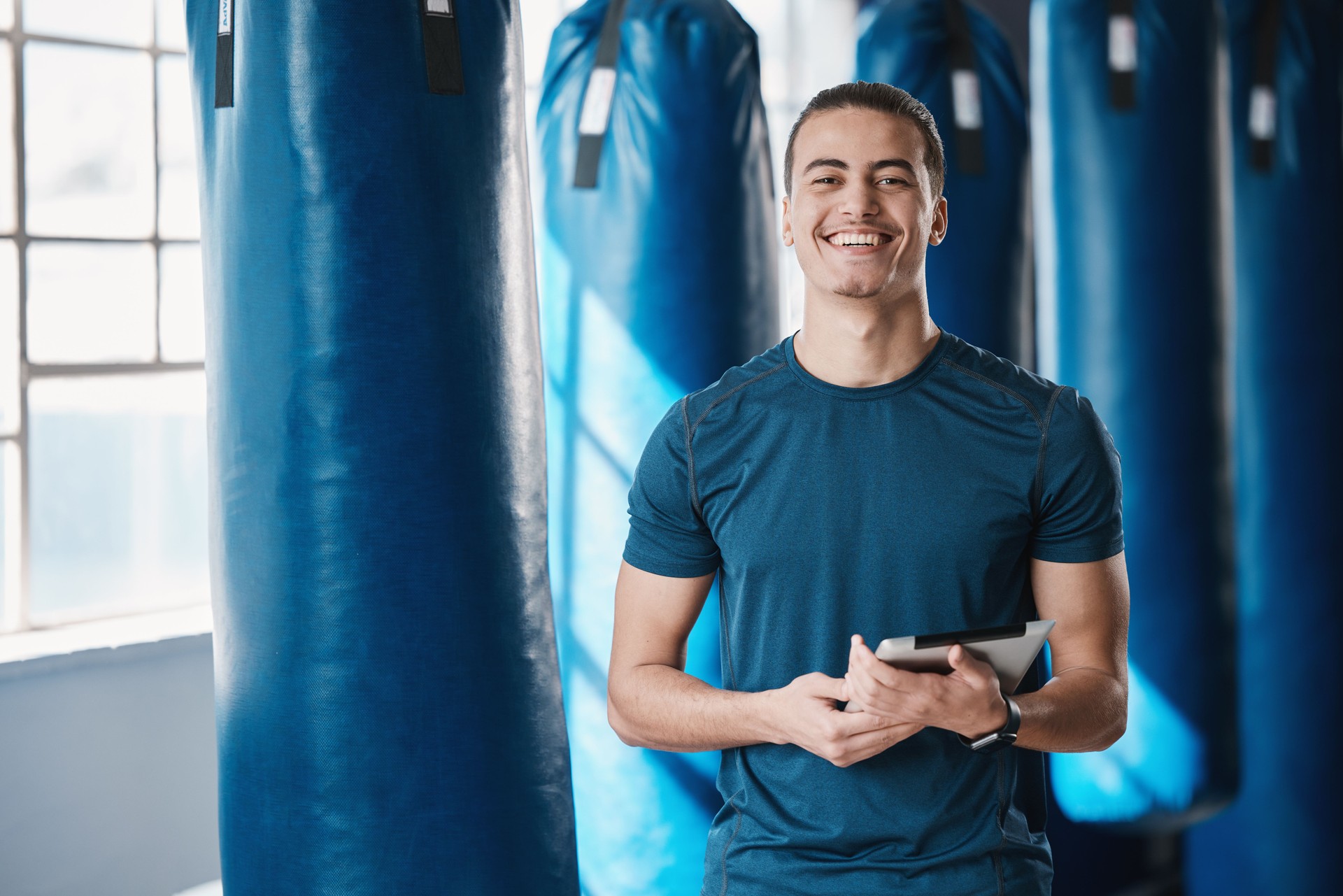 Fitness, man and gym coach with tablet ready for exercise class and training with a smile. Young male person, athlete and wellness center for personal trainer happy from workout with digital app