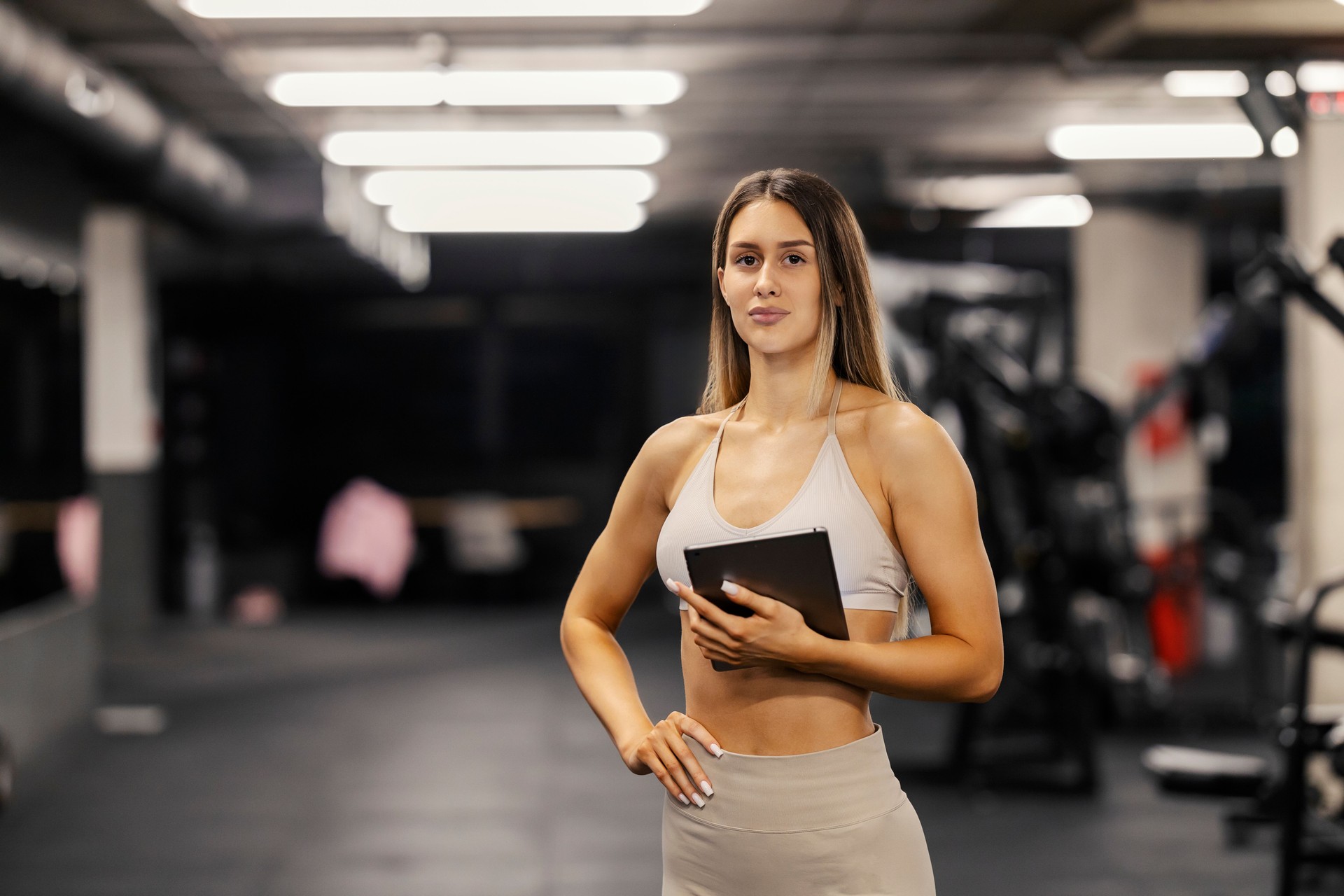 Portrait of fitness trainer standing at gym with tablet in hands.